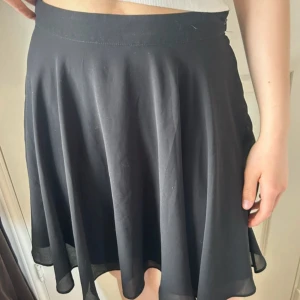 Svart kortkjol med dragkedja - Svart, flowy kortkjol med lätt utsvängd form och diskret dragkedja i sidan. Materialet känns lätt och följsamt. Skriv vid intresse! 🌸