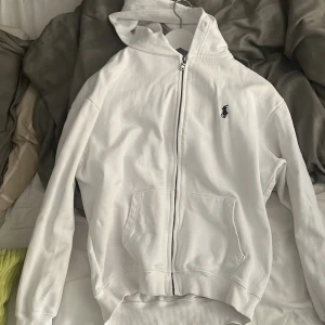 Vit hoodie från Polo Ralph Lauren - Vit hoodie från Polo Ralph Lauren med dragkedja och klassisk logga på bröstet. Perfekt för en clean och stilren look. Tillverkad i mjuk bomull som känns skön mot huden. Storlek Large fast känns som Medium. Ungefär 3 månader gammal.