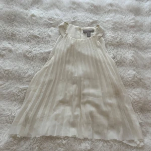 Vit plisserad blus från H&M - Säljer en luftig och snygg vit blus från H&M med plisserat tyg och ärmlös design. Toppen har rund halsringning och ett flowy fall som ger en fräsch och stilren look. Perfekt till sommaren när du vill ha något lätt och trendigt.