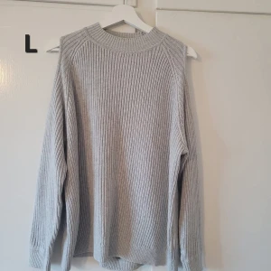 Ljusgrå ribbad stickad tröja - Säljer en ljusgrå stickad tröja med ribbad struktur och rund hals. Tröjan har lång ärm och en relaxed passform, perfekt för lager på lager. Enkel och stilren design som funkar till många outfits.