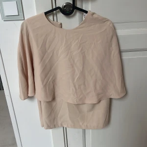 Beige blus från Stylein - Säljer en stilren beige blus från Stylein i storlek S. Blusen har en lös passform med rund halsringning och trekvartsärm. Den har ett lager-på-lager-utseende och är tillverkad i ett lätt, flowy material som ger en snygg siluett.
