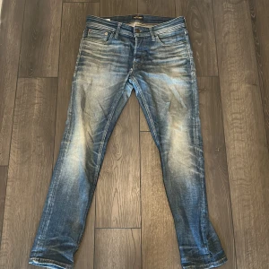 Blå jeans från Jack & Jones - Snygga blå jeans från Jack & Jones med slitna detaljer och klassisk femficksdesign. Jeansen har normal passform och raka ben, med en cool tvättad look och läderpatch bak i midjan. Perfekta för en avslappnad stil.