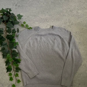 stickad tajt tröja (grå) - Snygg grå ribbstickad tröja från GANT med broderad logga på bröstet. Tröjan har rund halsringning och långa ärmar, perfekt för lager på lager. Skön och stilren modell som funkar till många olika outfits.