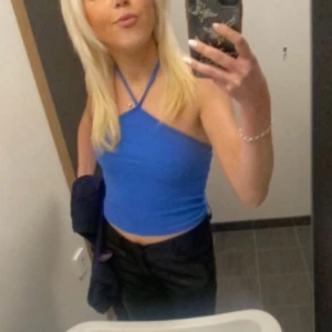 Blå croppad halterneck linnetopp - Säljer en blå croppad linnetopp med halterneck och smala axelband som korsas i nacken. Toppen är tight och har en enkel, stilren design. Från Nelly