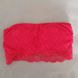 Röd spets bandeau från H&M - Säljer en snygg bandeau topp från H&M i stark röd färg (mörkare röd i verkligheten men svårt att fånga på bild). Toppen är helt ärmlös och täckt av blommig spets med transparent nederkant. Stödskenor i sidan och uttagbara inlägg. Bomullsblandning i innertyget så den är skön mot huden. Använd max 3ggr. Pris kan diskuteras 
