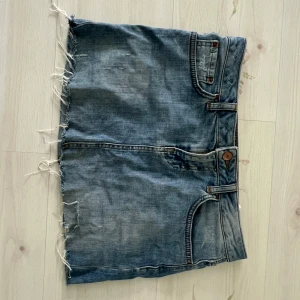 Blå jeanskjol med fransig kant - Säljer en blå jeanskjol från LTB med rå, fransig nederkant och klassiska fickor både fram och bak. Kjolen har bälteshällor och knäppning med knapp och dragkedja. Perfekt för dig som gillar en avslappnad och cool stil.
