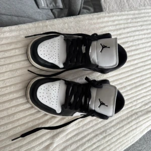 Nike Air Jordan 1 Low svart/vit - Snygga Nike Air Jordan 1 Low sneakers i svart och vitt med klassisk Jumpman-logga på plösen. Skorna har svart snörning, perforerad tåbox och robust gummisula. Perfekta för dig som gillar streetstyle och vill ha en ikonisk look.