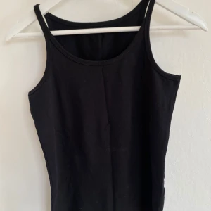 Svart enkel linnetopp - Svart basic linnetopp med smala axelband och rundad halsringning. Perfekt att styla lager på lager eller bära som den är. Gjord i mjuk bomull som känns skön mot huden.