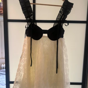 Svart och vit spetsklänning med volang - Unik supersöt miniklänning som jag älskar men tyvärr inte använder så mycket. Köpt i en liten butik i Köpenhamn, därav priset. Kjolen är vit med broderad spets och swirlmönster. Rosetterna är avtagbara men ger verkligen något extra till klänningen💕