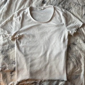 Vit ribbad topp från ONLY - Vit ribbad topp från ONLY med korta ärmar och rund halsringning. T-shirten har en tight passform och är tillverkad i mjukt bomullsmaterial. Perfekt att styla med jeans eller kjol för en clean look.