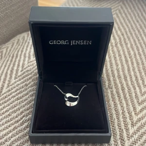 Georg Jensen Silverhalsband  - OANVÄNT Snyggt halsband från Georg Jensen med ett modernt, böljande i ett hjärta i blankt silver. Kedjan är tunn och elegant. Perfekt för dig som gillar minimalistisk design med en twist.