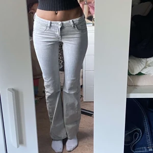 Ljusgrå low bootcut jeans - Säljer ett par ljusgrå jeans med bootcut-modell och klassisk femficksdesign. Jeansen har låg midja och är tillverkade i mjukt denimtyg som sitter snyggt över höfterna och låren. Perfekta för dig som gillar en retro vibe och vill ha ett par jeans som sticker ut.