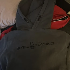 Mörkgrå hoodie från Sail Racing XL - Säljer en mörkgrå hoodie från Sail Racing i storlek XL. Tröjan har stor huva med snörning och Sail Racing-logga broderad på ryggen. Insidan är mjuk och fleecefodrad för extra komfort. Perfekt för chill dagar eller när du vill ha en sportig look.