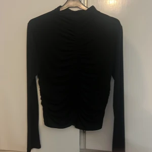 Svart långärmad topp från Gina Tricot - Säljer en svart långärmad topp från Gina Tricot i storlek L. Toppen har snygga rynkade detaljer framtill som ger en cool och trendig look. Materialet känns mjukt och stretchigt, perfekt för dig som gillar stilrena plagg med en twist.