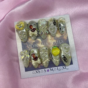 San (M);Medium Almond - Set med handgjorda press-on naglar i gulcateye bas med 3D dekorationer som pärlhjärtan, rosetter, stenar, citron och text, bild av Ateez San. Mix av motiv och former, vissa med holografiska effekter och små pärlor. Perfekt för dig som vill sticka ut med unika naglar. I storlek M: 16 mm, 12 mm, 12,5 mm, 11,5 mm, 10 mm 
