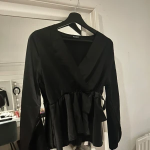 Svart omlottblus från Missay - Stilren svart omlottblus från Missay med v-ringning och knyt i midjan. Blusen har långa ärmar och volangdetalj nedtill. Favorit och funkar verkligen till alla tillfällen!!