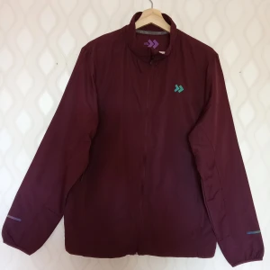 Vinröd vindjacka med dragkedja - Säljer en vinröd vindjacka med hel dragkedja och meshfoder. Jackan har två fickor med dragkedja och en stilren logga på bröstet. Perfekt för blåsiga dagar och enkel att slänga på sig över en hoodie. Snygg och funktionell design.                                                  Kan skickas med extra pris via post.