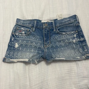Mönstrade jeansshorts från Hollister - Snygga blå jeansshorts från Hollister med fint mönster framtill och slitna detaljer. Klassisk femficksmodell, råa kanter och låg midja. Perfekta för sommaren.