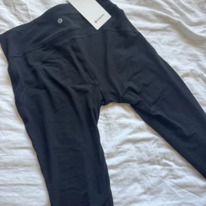 Svarta Groove Nulu Flared Pants Lululemon - Svarta Groove Nulu Flared Pants från Lululemon med hög midja och utsvängda ben. Tillverkade i supermjuk Nulu-tyg med Lycra för extra stretch och fukttransport. Byxorna har en bakficka och en bred, bekväm linning som sitter skönt. Perfekta för yoga, träning eller att ha hemma! 