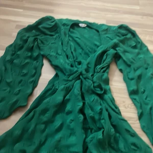 Grön omlottklänning från Bubbleroom - Snygg grön omlottklänning från Bubbleroom i storlek 40. Klänningen har långärmade puffärmar med resår vid ärmslut, v-ringad hals och knyt i midjan. Materialet är lätt och har en cool textur med diskreta prickar för extra attityd.