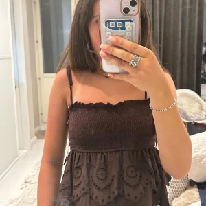 Brun kortklänning från Stradivarius - Supersöt brun klänning från Stradivarius med smockad överdel och tunna justerbara axelband. Kjoldelen har broderade detaljer och volanger som ger en boho-vibe. Perfekt för varma dagar och enkel att styla med smycken eller sneakers. 🥰🥰