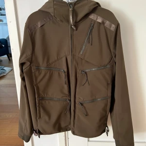 Khaki soft Shell jacka med goggles från C.P. Company - Storlek 48 motsvarar M. Sparsamt använd så jackan är i mycket bra skick. Ända skavanken är hängöglan som är trasig (bild 4)