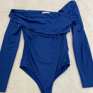 Blå offshoulder topp från Zara - Snygg blå offshoulder topp från Zara med lång ärm och figurnära passform. Toppen har en bred, vikt kant över axlarna som ger en cool och trendig look. Perfekt att styla med höga jeans eller kjol för en chic outfit.