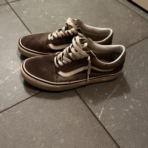 Gråa Vans Old School sneakers - Säljer ett par klassiska Vans Old School sneakers i gråa med vit sula och ikonisk sidorand. Skorna har snörning, rund tå och ovandel i mocka och canvas. Perfekta för dig som gillar en tidlös och avslappnad stil.
