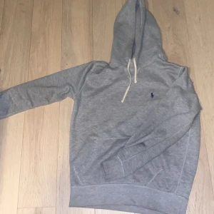 Grå hoodie från Polo Ralph Lauren - Säljer en stilren grå hoodie från Polo Ralph Lauren med klassisk huva och dragsnören. Tröjan har en liten blå logga broderad på bröstet. Storlek S passar allt från 170-180 