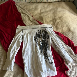 Vit offshoulder tröja med tryck från Lindex - Cool vit offshoulder tröja från MOM by Lindex i storlek S. Tröjan har ett svart konstnärligt tryck med ansikte på framsidan och långa ärmar. Materialet är mjuk bomull och passformen är normal. Perfekt för dig som gillar unika prints och vill sticka ut.