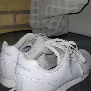 Vita Reebok sneakers i skinn - Klassiska vita sneakers från Reebok med stilren design och diskret logga på sidan och hälen. Skorna har snörning, rund tå och är tillverkade i slätt skinn. Perfekta för en clean och sportig look.