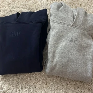 Grå och marinblå hoodie från GAP med broderad logga - Säljer en grå och en marinblå hoodie från GAP med broderad logga på bröstet. Tröjan har huva, magficka och långa ärmar. Mjuk insida med fleece och till både tjej och kille. Skulle säga att den passar storlek 146-152. Säljer för att den är för liten! Båda för 70kr!!!