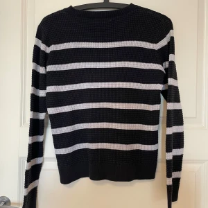 Svart och vitrandig stickad tröja - Säljer en svart stickad tröja med vita horisontella ränder. Tröjan har långärmad passform och en grovstickad struktur som ger en cool och avslappnad vibe. Perfekt för dig som gillar klassiska mönster med en modern twist.
