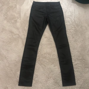 Svarta skinny jeans från Levis - Säljer ett par svarta skinny jeans från Levis med snyggt glansig finish. Klassisk femficksmodell med svarta detaljer och knapp med Levis-logga. Jeansen har smal passform och är tillverkade i stretchigt material för extra komfort. Storlek M men funkar som  S 