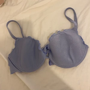 Calzedonia Ljuslila glittrig bandeau bikiniöverdel  - Supersöt ljuslila bandeau bikiniöverdel med glittrigt tyg och volangkant. Knytning både i ryggen och runt nacken för perfekt passform. Kan placeras och knytas på två olika sätt, visas på bild. Kuporna är vadderade och ger bra stöd. Storlek L/38 och använd  1 gång i havet och tvättad även 1 gång, riktigt bra skick som ny. 