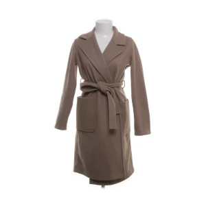 Beige omlottkappa från Amisu, stl 34 - Snygg beige kappa från Amisu i omlottmodell med bälte i midjan och stora fickor framtill. Långärmad och med klassisk krage, perfekt för dig som gillar stilrena och enkla plagg. Passar dig som vill ha en tidlös look under höst och vinter.