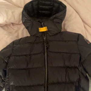 Svart dunjacka Parajumpers Sheen - Säljer en svart dunjacka från Parajumpers, modell Sheen. Jackan har en hög krage, huva och dragkedja framtill. Klassisk gul detalj vid halsen och patch på ärmen. Perfekt för kalla dagar och riktigt snygg passform.💞 nästan helt ny. Köpte den i vintras. Har använt den i vinter och inget mer så är det nästan helt ny, såklart äkte, skriv om ni vill ha fler bilder eller om ni har frågor 💞💕