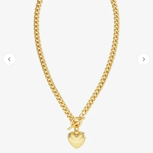 Guldfärgat halsband med hjärthänge - Snyggt halsband i guldfärg med kraftig kedja och ett hjärtformat hänge. Halsbandet har ett dekorativt T-lås framtill som ger en trendig look. Perfekt accessoar för att lyfta din outfit.