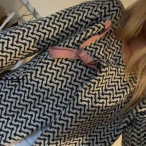 Odd Molly zigzag kofta med rosa knyt - Säljer en snygg kofta från Odd Molly med svartvitt zigzag-mönster och en rosa knytband vid halsen. Koftan är stickad och har lång ärm, perfekt för dig som gillar unika detaljer och mönster. Passar dig som vill ha något som sticker ut i garderoben.