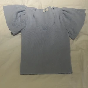 Ljusblå topp med puffärm från ONLY - Supersöt ljusblå topp från ONLY i stickad polyester med fyrkantig halsringning och stora puffärmar. Den har en slim passform och ribbad struktur som ger en modern vibe. Perfekt att styla med jeans eller kjol för en trendig look.