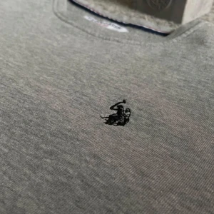 Grå polo tröja - Snygg grå långärmad tröja från U.S. Polo Assn ( märke av Ralph lauren). med klassisk rund hals och svart broderad logga på bröstet. Tröjan har en enkel och clean look, perfekt för chill dagar. Materialet är mjuk bomull som känns skönt mot huden. Vid frågor tveka verkligen inte att höra av dig!😊