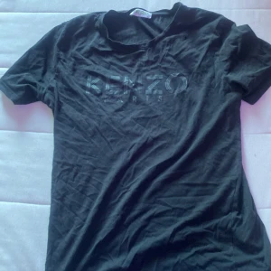 Svart Kenzo t-shirt med tryck - Svart t-shirt från Kenzo med coolt logotryck på bröstet. Klassisk rund hals och korta ärmar. T-shirten är gjord i mjuk bomull och har en normal passform. Perfekt för dig som gillar stilrena och trendiga märkesplagg.