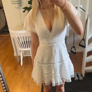 Vit spetsklänning med volang och omlott - Superfin vit kortklänning med spetsdetaljer, omlott-v-ringning och volangkant. Klänningen har korta ärmar och dragkedja i ryggen. Perfekt för studenten! Aldrig använd med prislapp kvar!💞💞