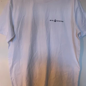 Vit t-shirt från Sail Racing - Säljer en klassisk vit t-shirt från Sail Racing med liten svart logga tryckt på bröstet. T-shirten har rund hals och korta ärmar, perfekt för en enkel och stilren look.