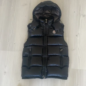 Moncler bormes down väst - Säljer en glansig väst från Moncler med avtagbar huva. Perfekt för dig som vill ha en snygg väst som man både kan använda under kalla och varma dagar. Passar perfekt för någon som är 175-190 lång och väger 60-80. Är i bra skick utan några synliga defekter. Använd några månader.