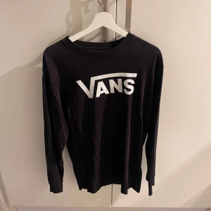 Svart långärmad tröja från Vans - Svart långärmad tröja från Vans med stor vit logga framtill. Klassisk rund halsringning och rak passform. Perfekt för en avslappnad streetstil.