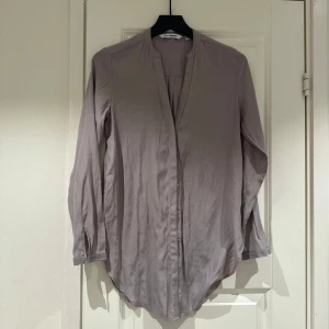 Ljusgrå långärmad skjorta från KappAhl - Säljer en stilren ljusgrå skjorta från KappAhl med lång ärm och knappar framtill. Skjortan har en mjuk, flowy känsla och klassisk krage utan slag. Perfekt för en clean och enkel look.