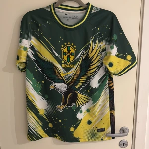 Brasilien fotbollströja med örnmotiv - Snygg Brasilien fotbollströja från Nike med stort örnmotiv på både fram- och baksida. Tröjan är grön med gula, vita och svarta detaljer samt Brasilien-emblem på bröstet. Tillverkad i Dri-FIT-material som andas.