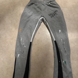 Grå mjukisbyxor från Gallery Dept. - Grå mjukisbyxor med resår i midjan från Gallery Dept. Byxorna har svarta och vita detaljer längs benen samt färgstänk i olika färger. Tryckt logga på vänster höft. Perfekta för en avslappnad stil.