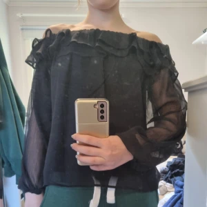 Svart offshoulder blus med volang från Gina Tricot - Säljer en svart, transparent offshoulder blus från Gina Tricot. Blusen har volangdetalj upptill och är tillverkad i ett tunt, lätt material. Perfekt för dig som gillar trendiga och feminina plagg. Har användit en gång.  Frakt ingår inte. Säljer för att jag har växt ur dem. Silikon band inbykt på axlarna så att tröjan inte glider ner. 